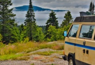 yellow volkwaen van parked at a lookout point overlooking an island with fog and trees