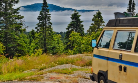yellow volkwaen van parked at a lookout point overlooking an island with fog and trees