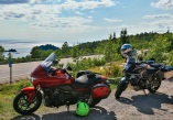 a red and black motorcycle parked at a roadside lookout stop, with view of water in background