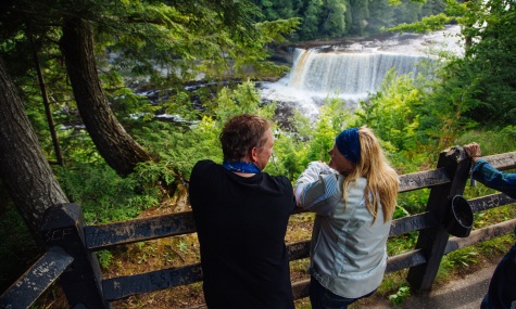 a couple standing behind a fence, overlooking a beautiful waterfall  with forest framing the picture