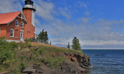 lighthouse with red brick building on the edge of a cliff surrounded by water